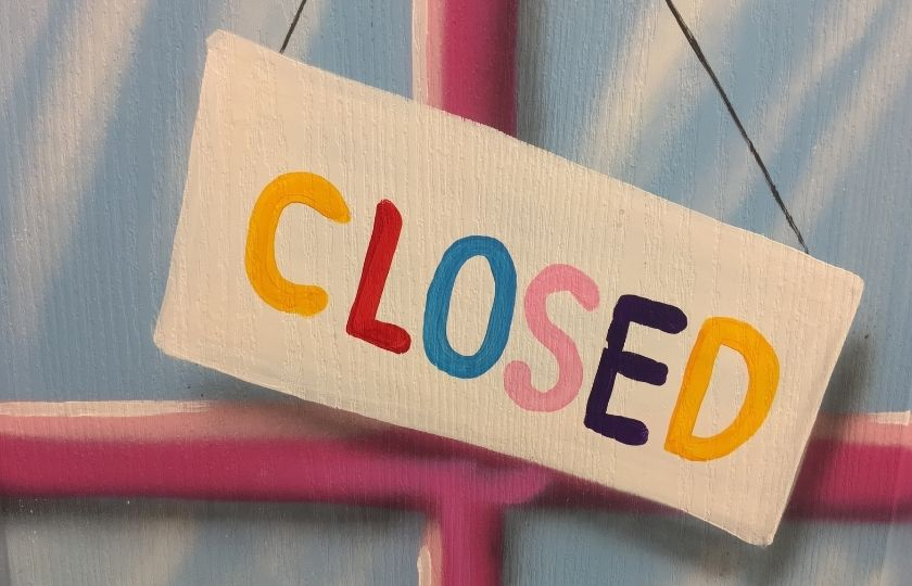 Sign saying 'closed' in multi-coloured text hanging against a window frame.